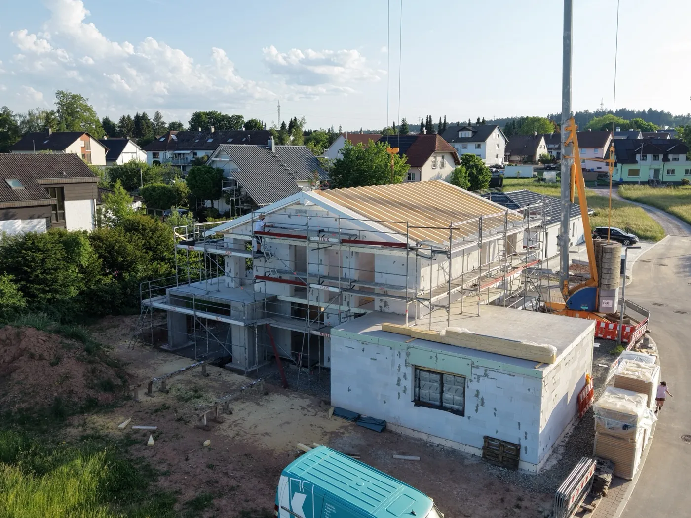 Luftaufnahme eines Rohbaus ohne Dach mit Gerüst, Baukran und Baumaterial