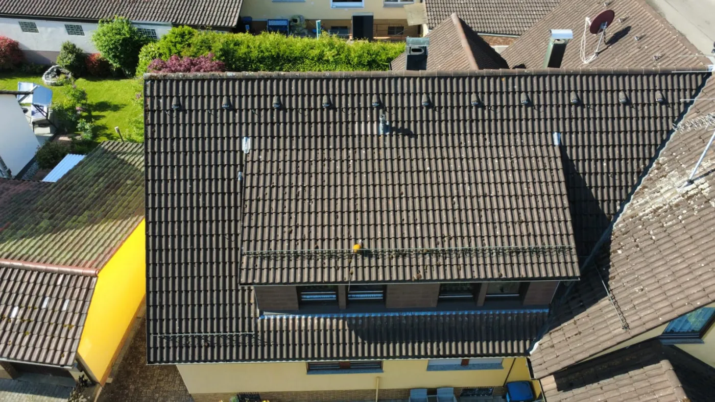 Luftaufnahme eines Einfamilienhauses mit hellem Dach und angrenzendem Grundstück