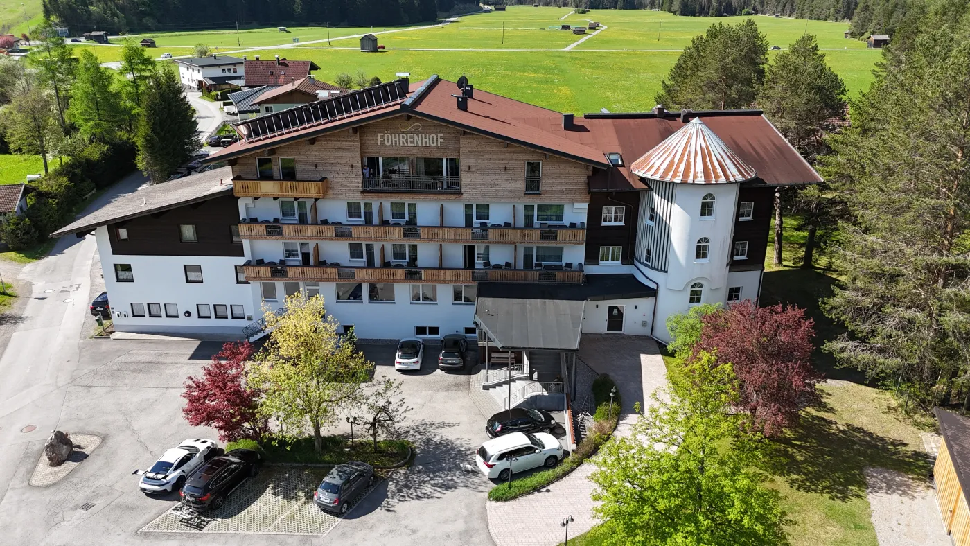 Luftaufnahme eines Hotelgebäudes im Alpenstil mit Vorplatz und parkenden Fahrzeugen
