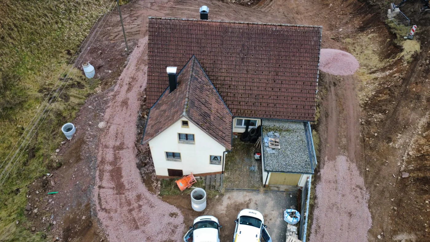 Luftaufnahme eines Wohnhauses mit braunem Dach, Garten und zwei Fahrzeugen in der Einfahrt