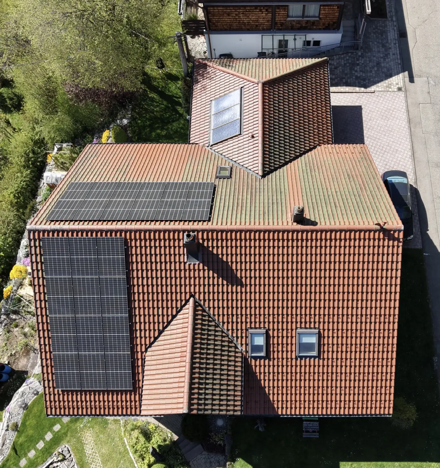 Luftaufnahme eines Wohnhausdachs mit Solarmodulen und angrenzendem Garten