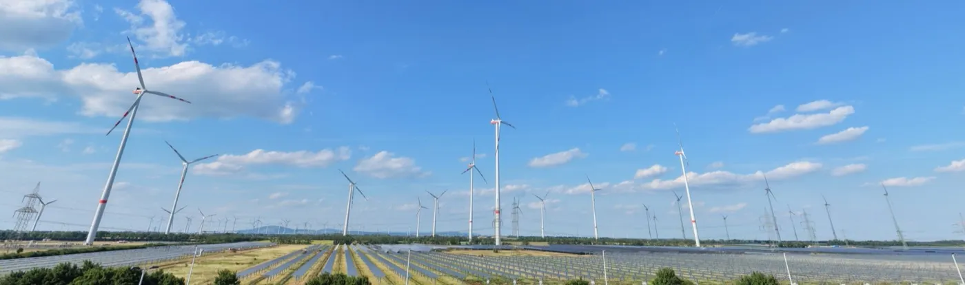 Luftaufnahme mehrerer Windkraftanlagen und einer Solaranlage, eng ausgeschnitten mit wenig Himmel