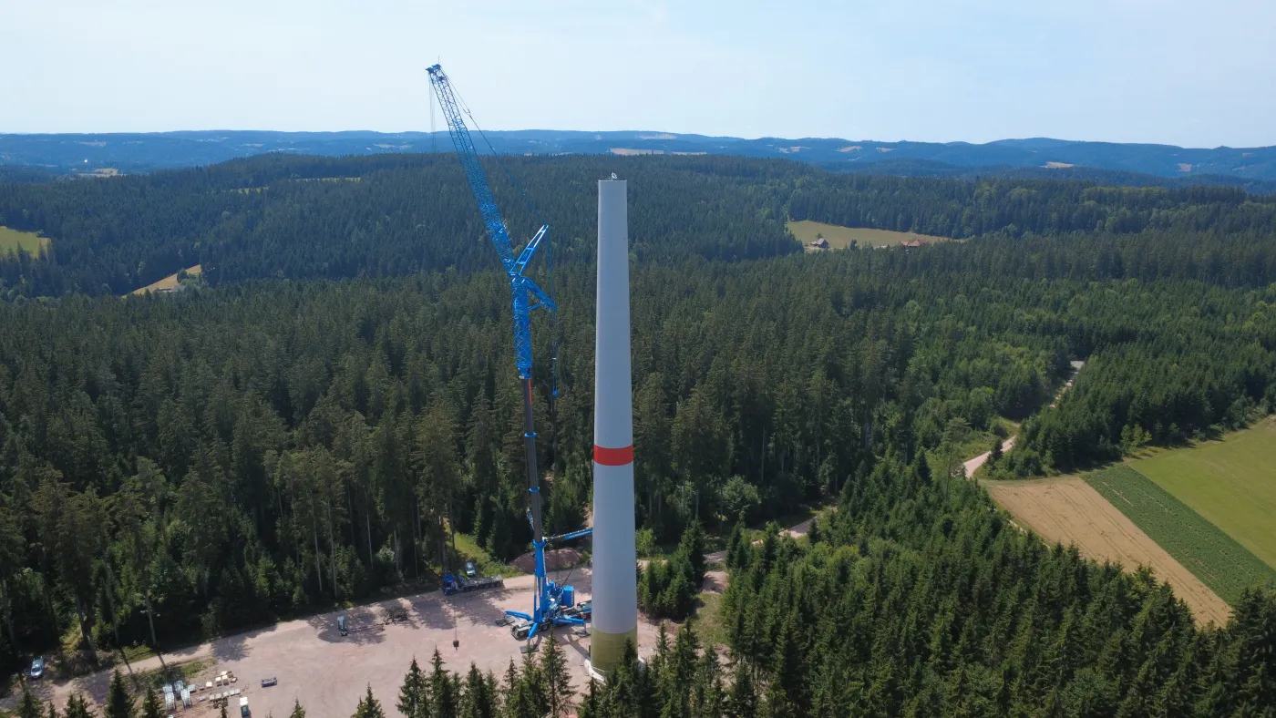 Luftaufnahme einer Windkraftanlage im Bau mit Kran am Waldrand