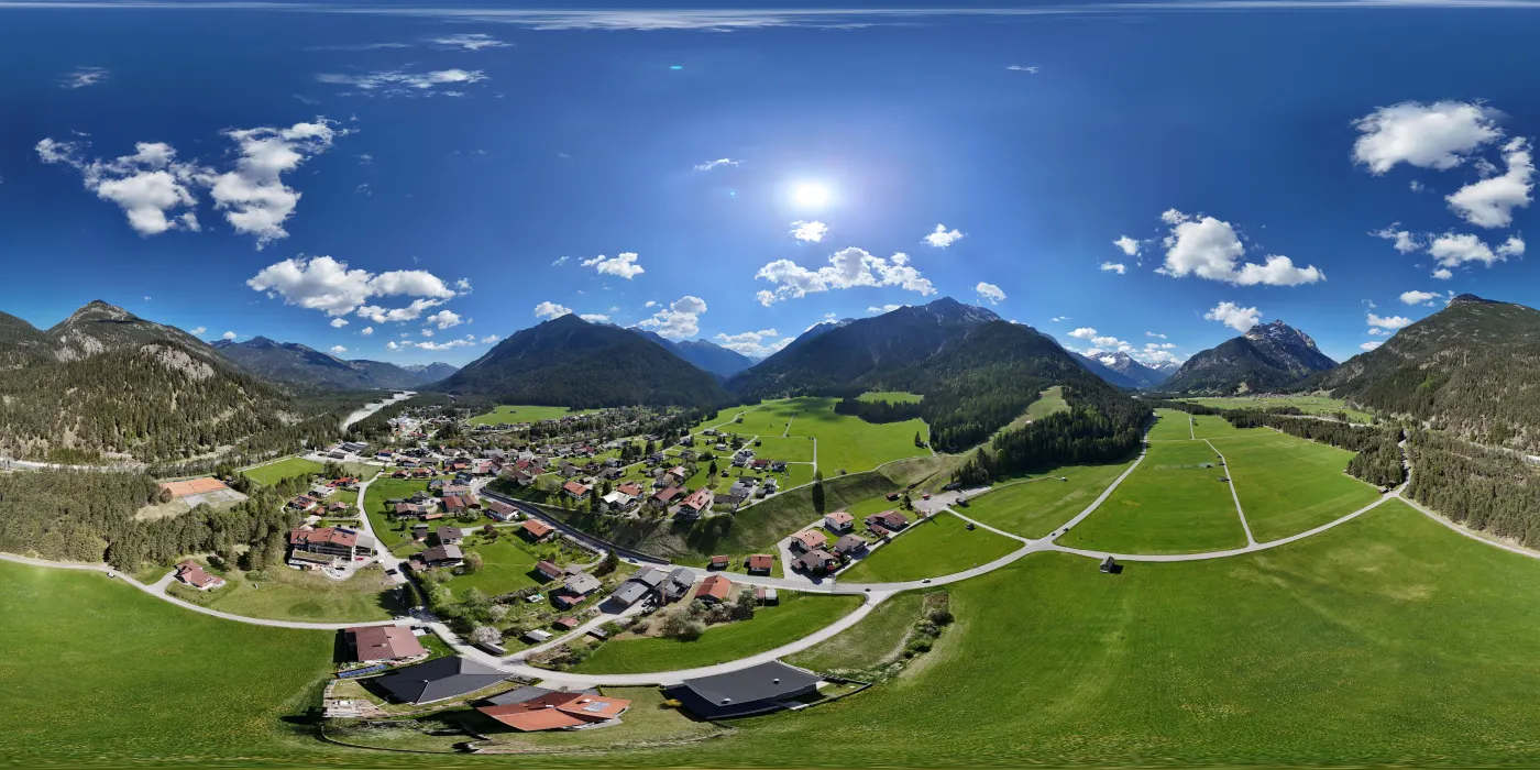 360-Grad-Panorama eines Dorfes mit umliegenden Wiesen und Bergen