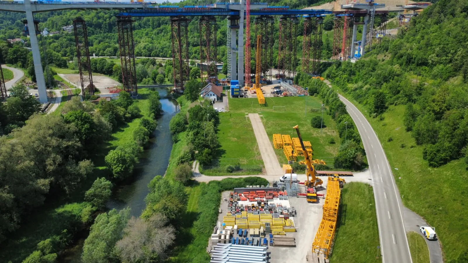Luftaufnahme einer im Bau befindlichen Talbrücke mit Baukränen entlang des Flusslaufs