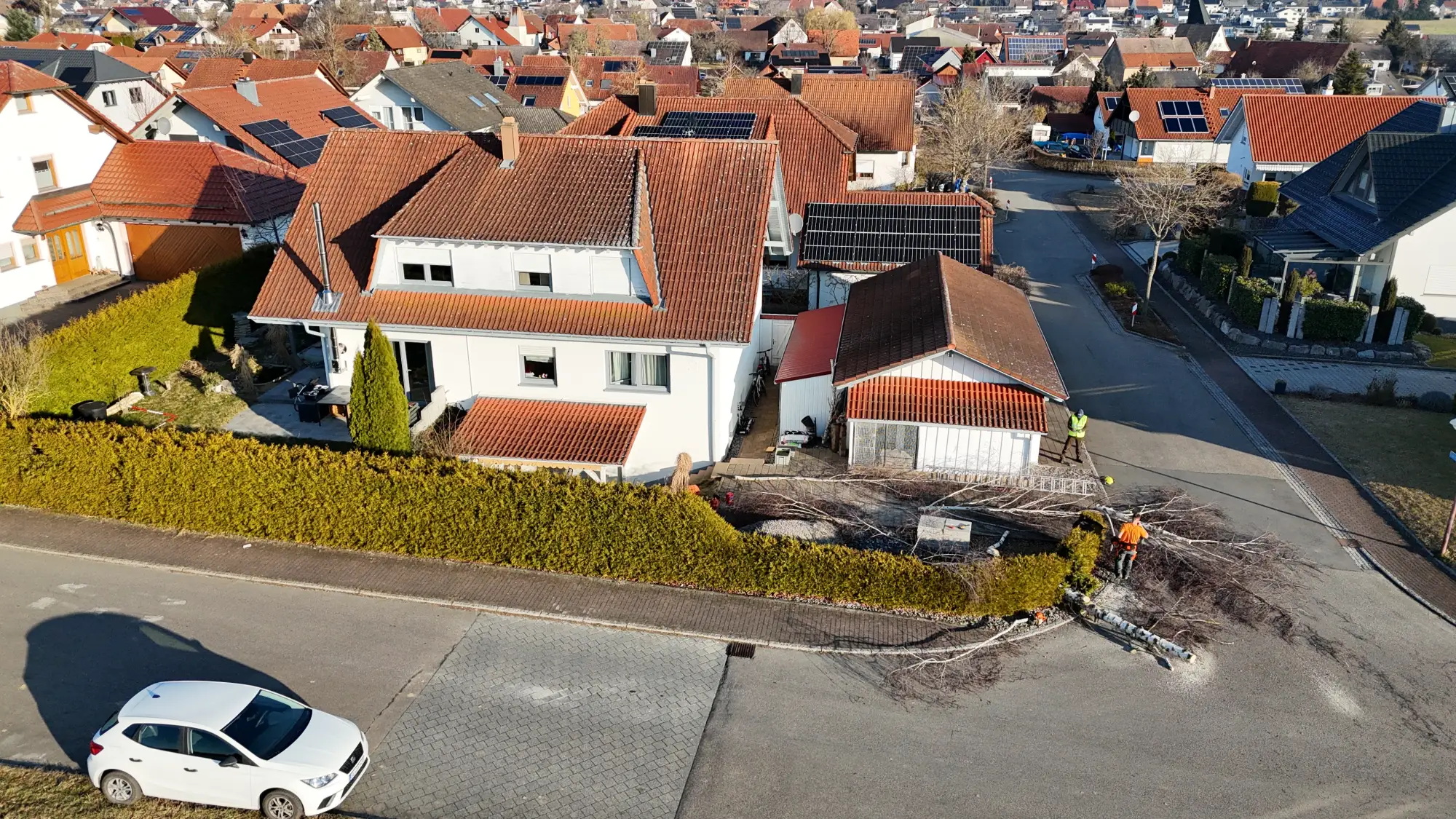 Luftaufnahme eines Einfamilienhauses mit Zufahrt, Garten und parkendem Auto in einer Wohnsiedlung