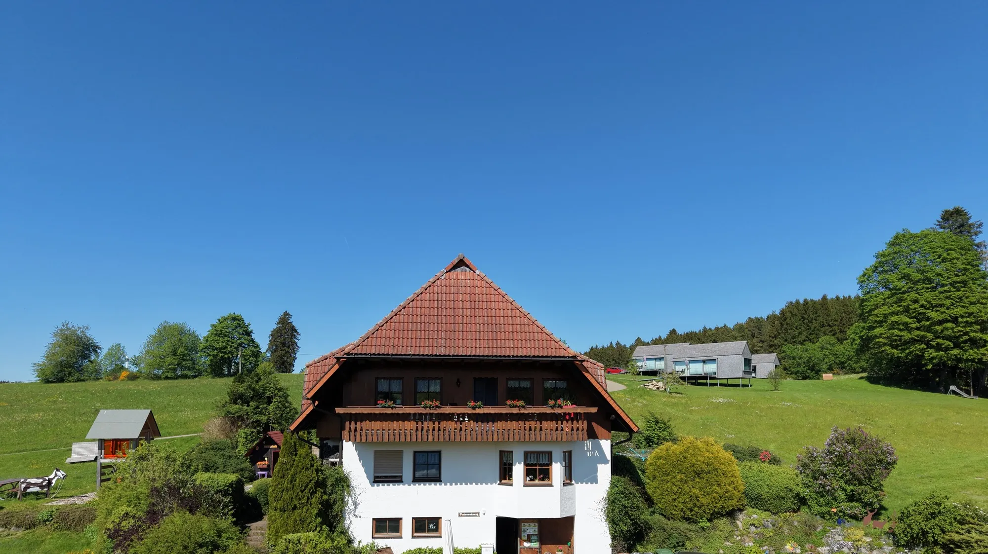 Luftaufnahme eines Schwarzwaldhofs mit weitläufiger grüner Wiese unter blauem Himmel, enger auf Haus und Himmel ausgeschnitten ohne Vorplatz