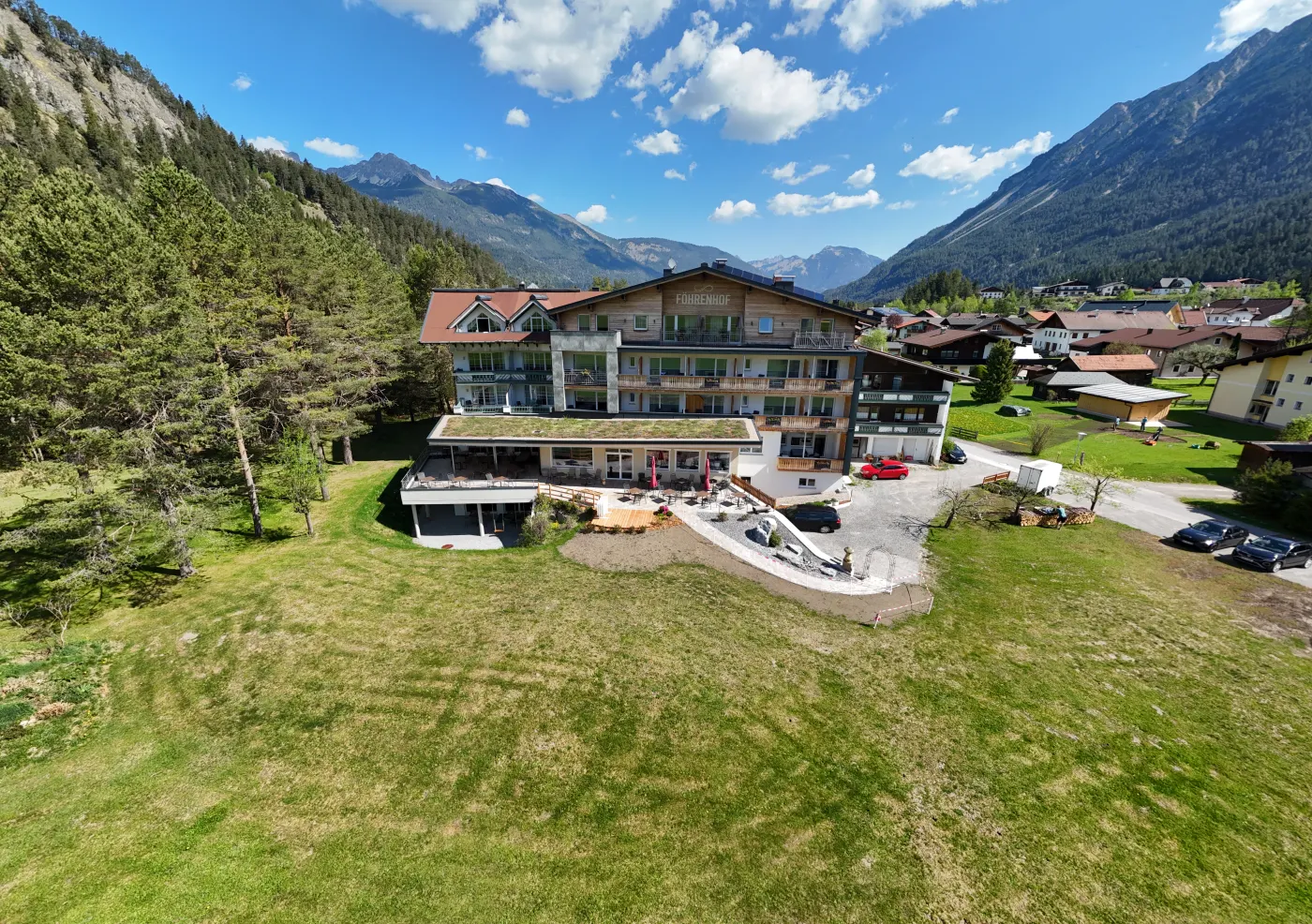360-Grad-Panorama eines Hotelgebäudes mit umliegender Wiesen- und Berglandschaft