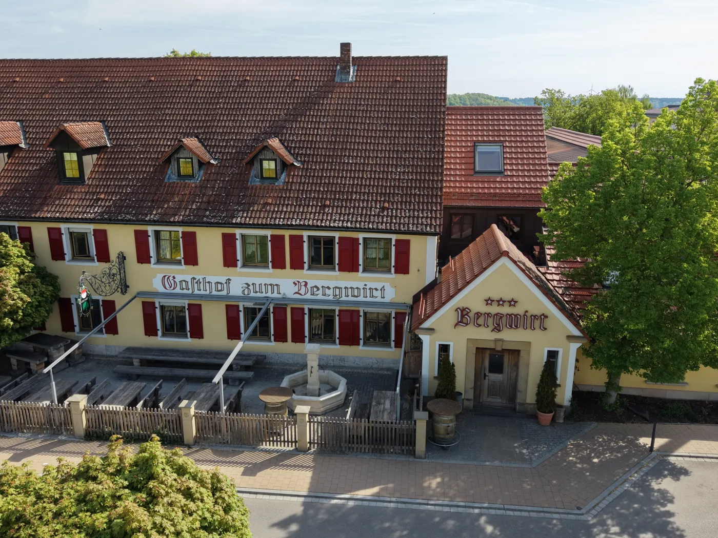 Luftaufnahme eines Gasthofs mit Vorplatz und parkenden Fahrzeugen